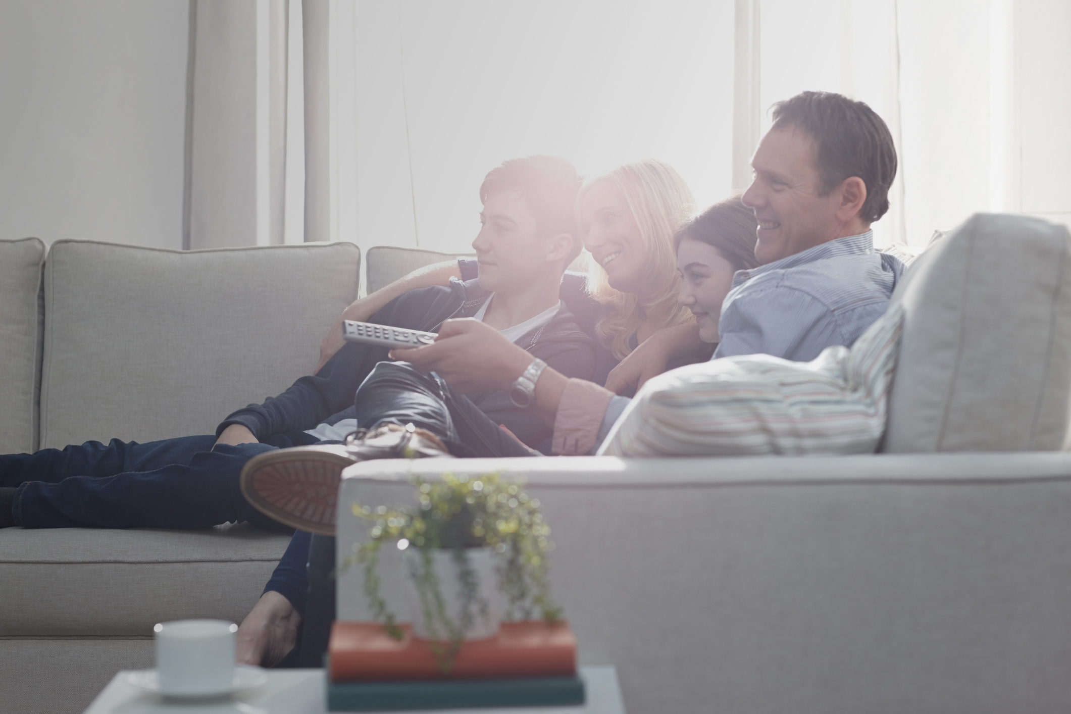 Family of four sitting together on sofa watching television – Indoors
